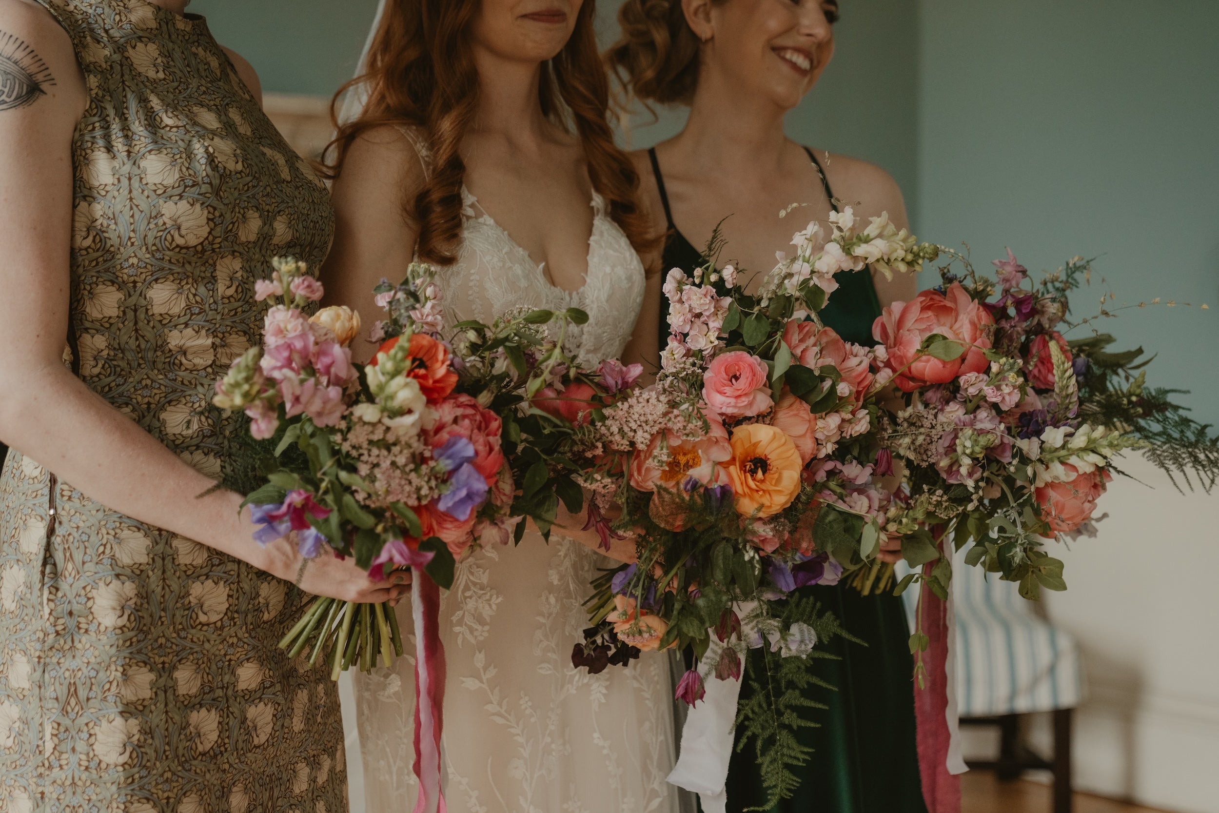 Three women holding large floral bouquets indoors.