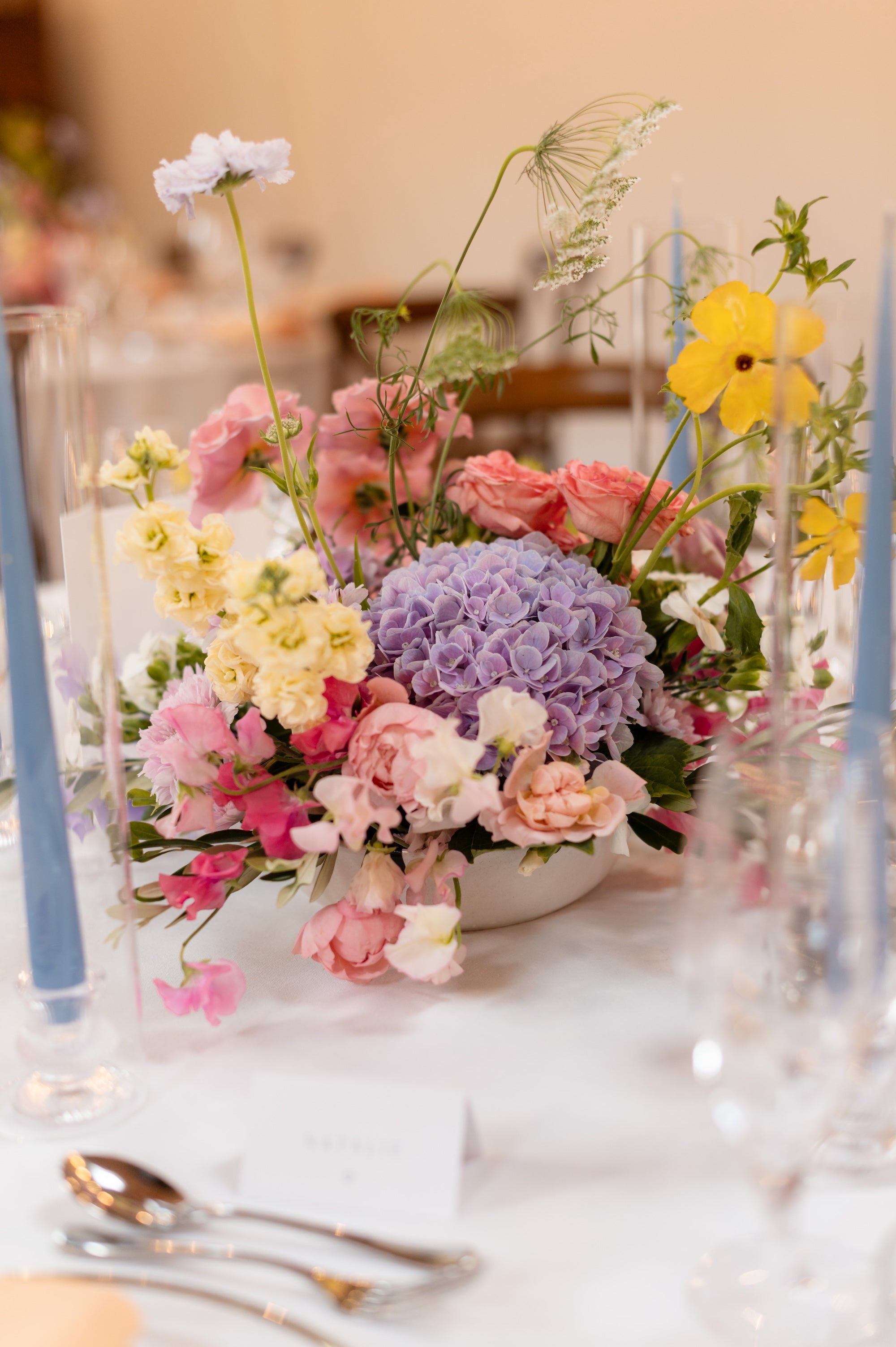 Colorful floral arrangement on a table with blue candles and cutlery.